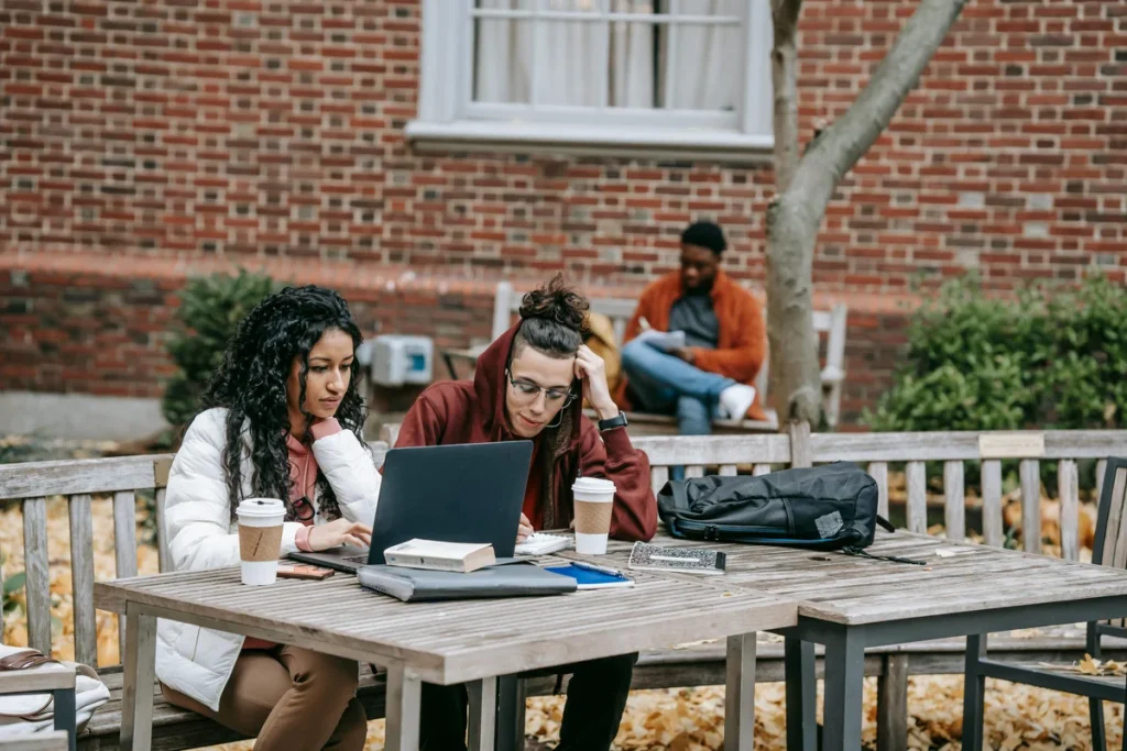 Students collaborating outdoors on campus with laptops and notes