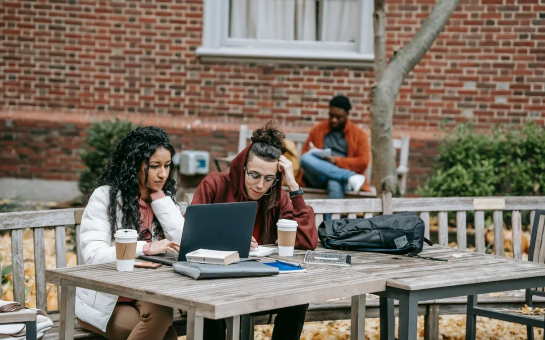 Students collaborating outdoors on campus with laptops and notes